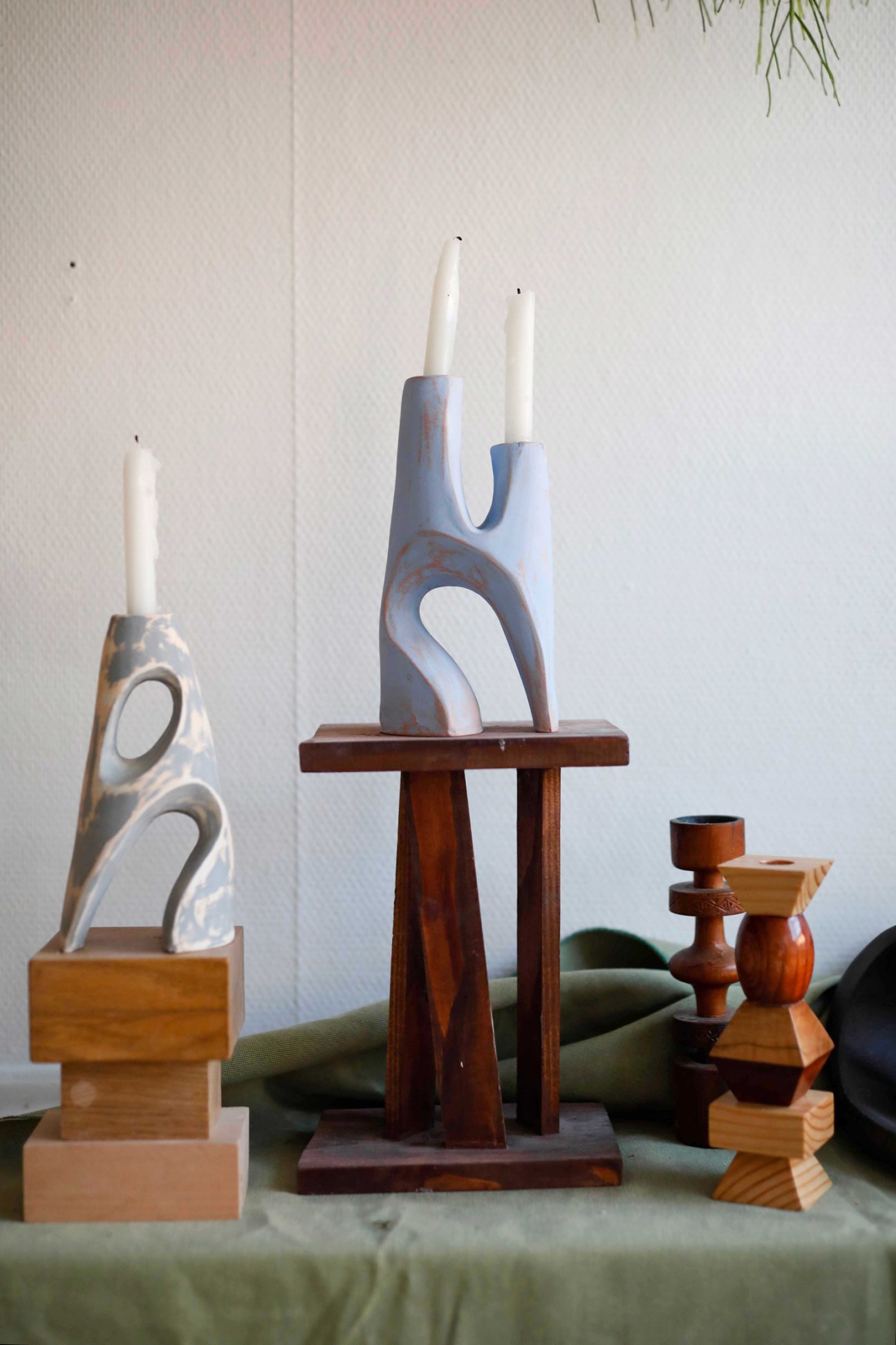 Contemporary ceramic sculptural candleholders with curved openings holding white candles on wooden surfaces