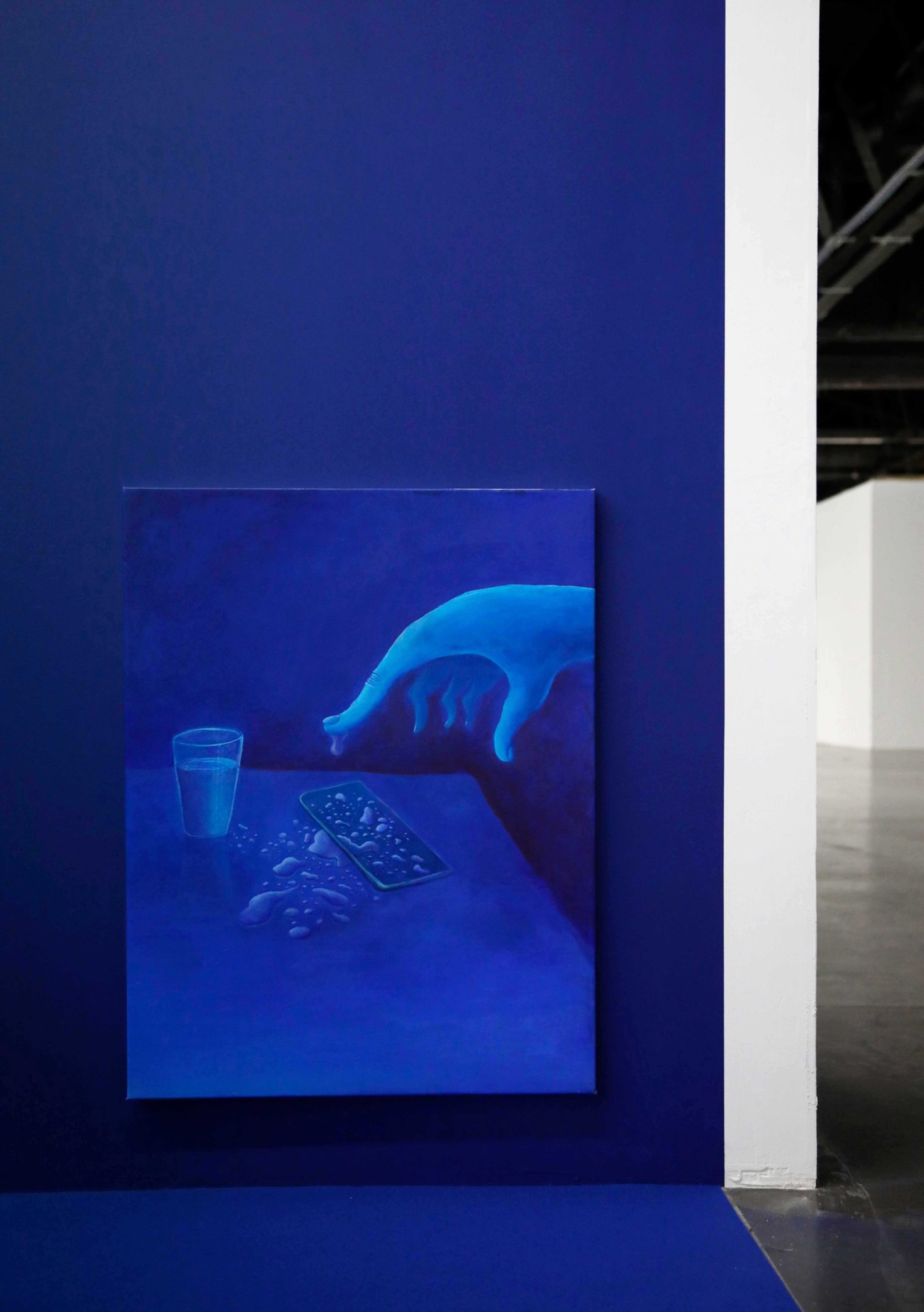 Abstract blue artwork with hand reaching toward electronic device and glass on table