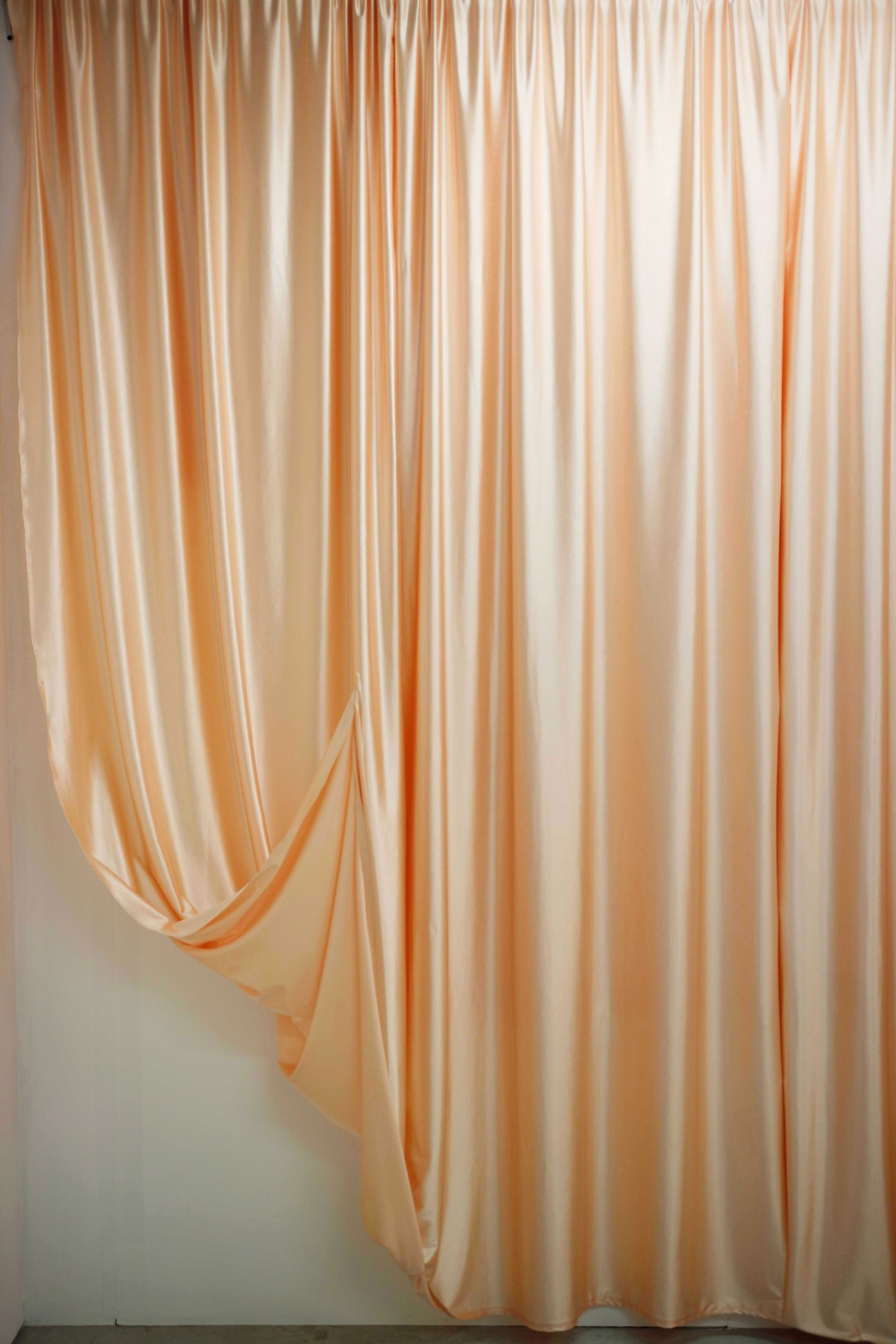 Flowing peach-colored satin curtain installation draped against white wall