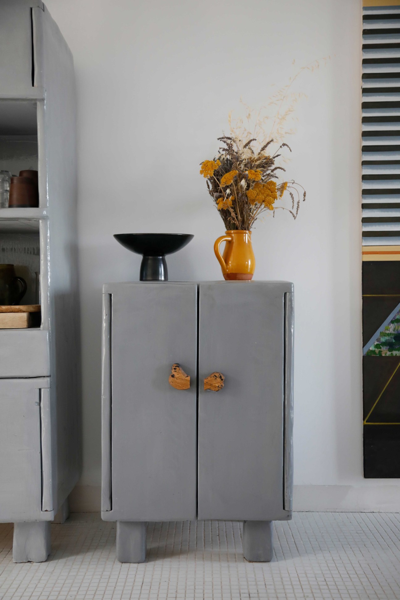 Gray cabinet with wooden knobs, black bowl and orange ceramic vase with dried flowers on top