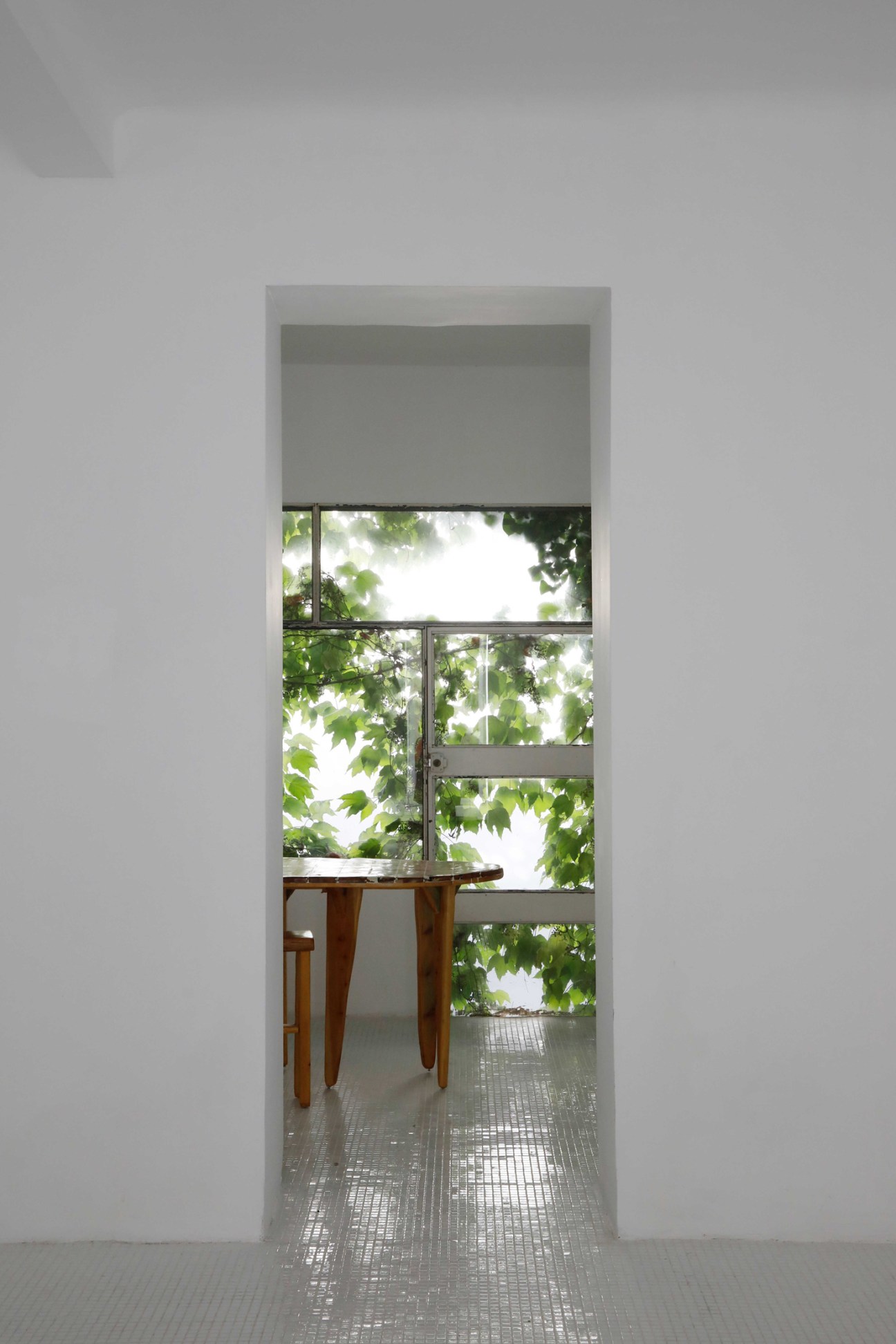 Dining table and chairs by artist Régis Jocteur Monrozier viewed through doorway with window and foliage beyond