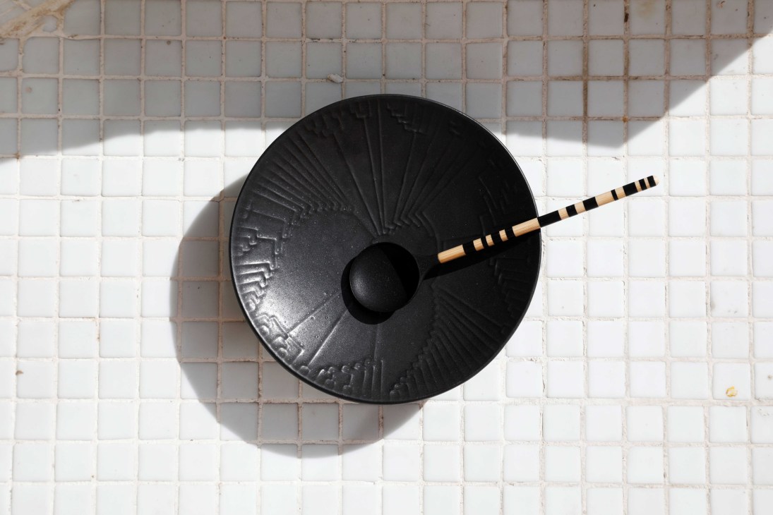 Black ceramic bowl with radiating pattern and wooden chopsticks on white tiled surface