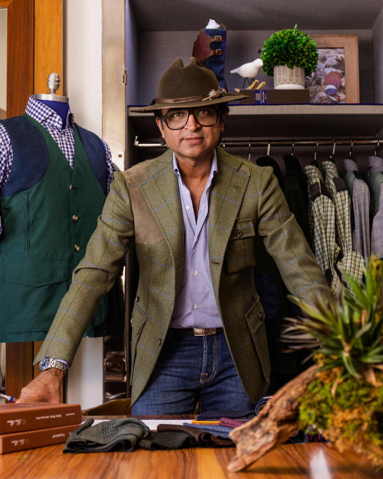Ed Shaikh of Field Shop sitting at a wooden table in his retail store wearing a green blazer and hat