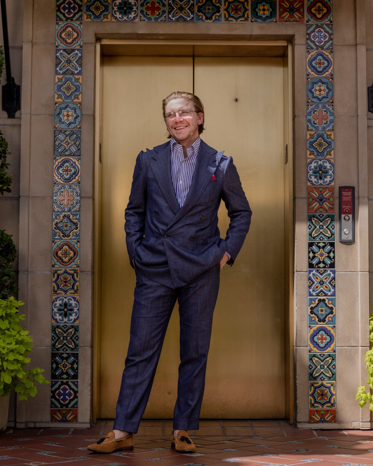 Blake Bridges of Hadleigh's wearing a navy double-breasted suit and striped shirt standing in front of decorative elevator
