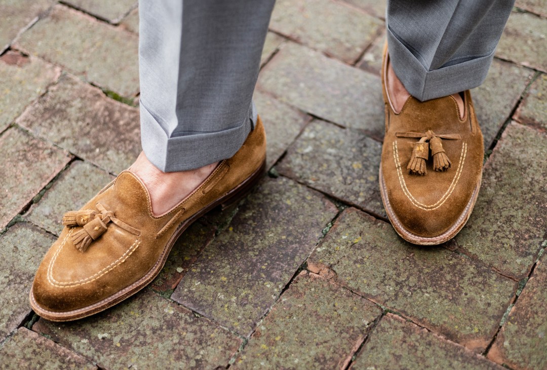 Close-up of brown suede tassel loafers with white contrast stitching on brick pavement