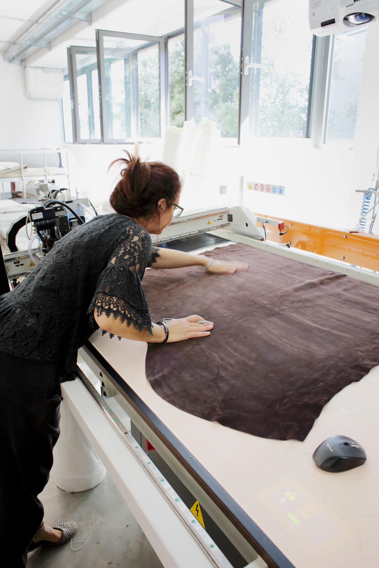 Woman operating laser cutting machine on dark leather material in Italian footwear factory