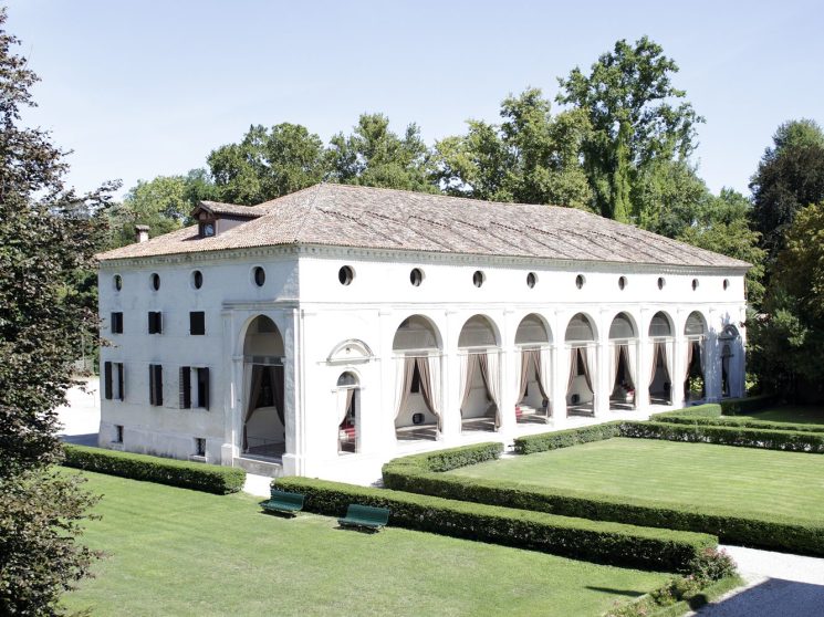 White Palladian villa with classical arched colonnade overlooking manicured formal gardens in Veneto, Italy