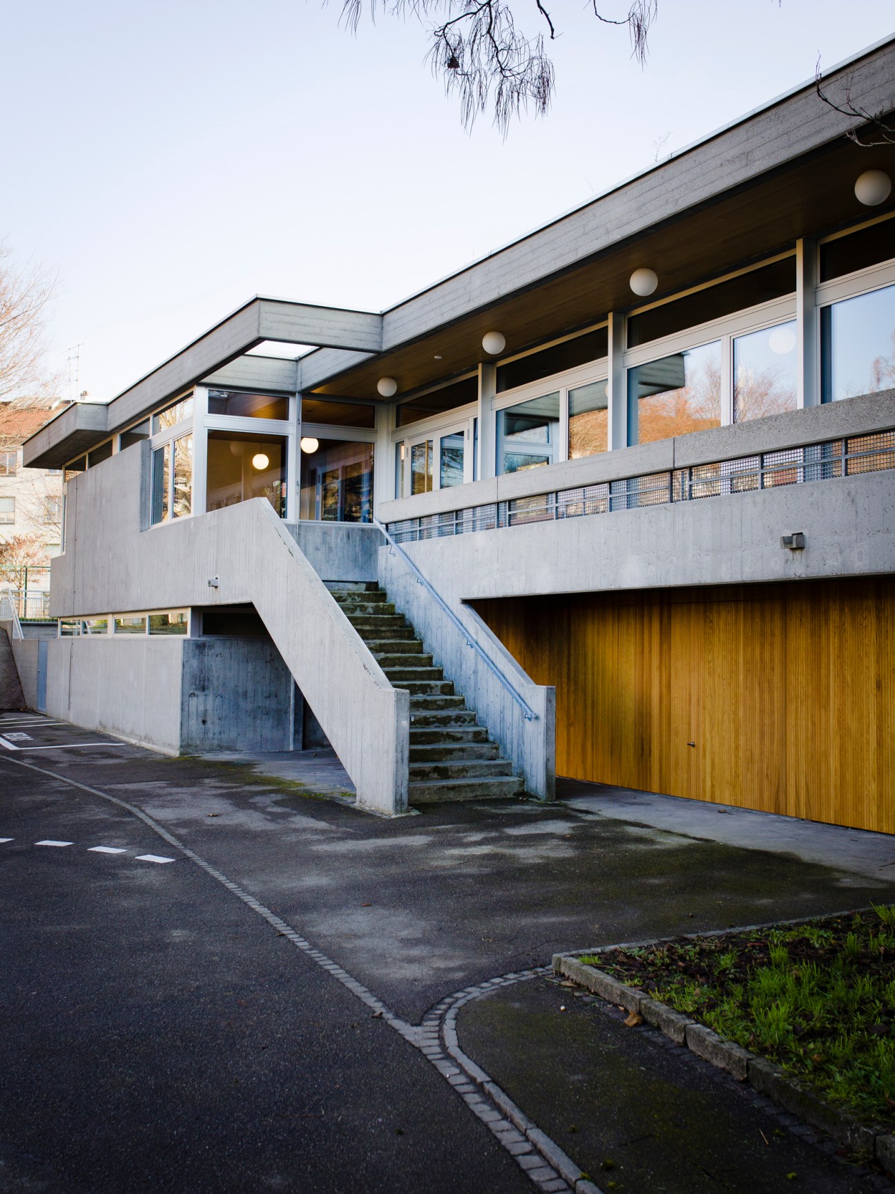 Modernist traffic school building in Basel with concrete stairs, wooden garage door, and glass-walled upper level