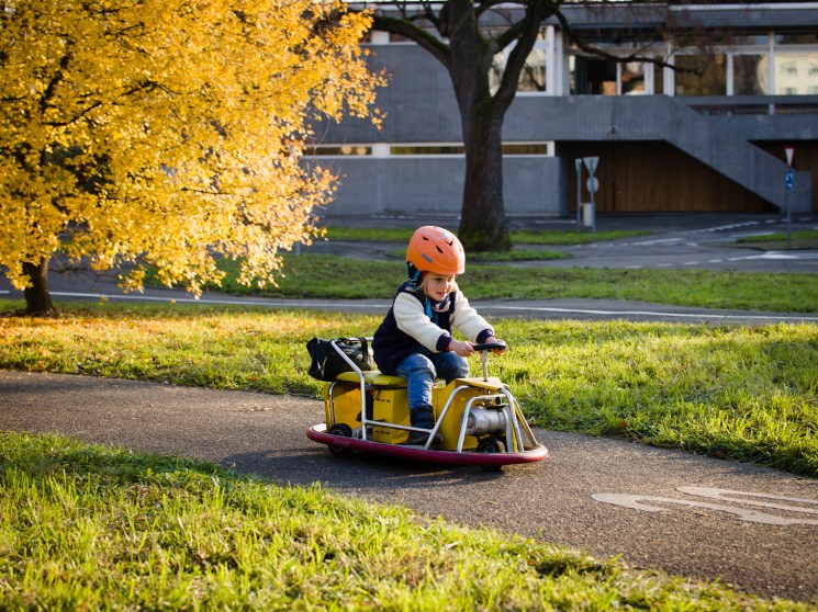 Child wearing orange helmet riding yellow go-kart vehicle on miniature road in Basel traffic garden