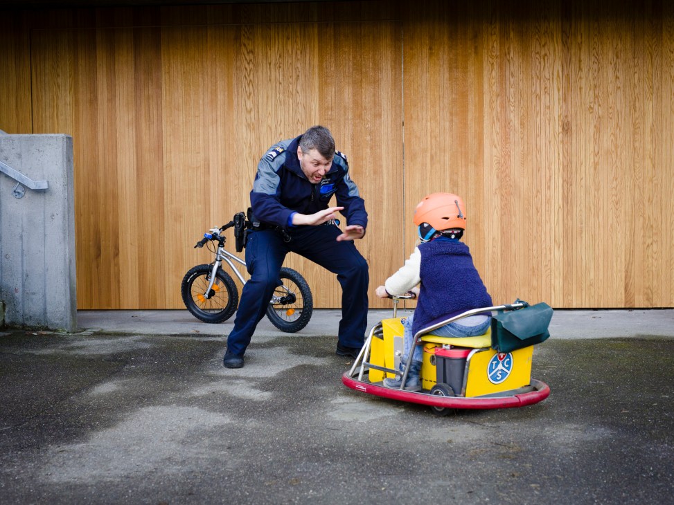 Adult instructor gesturing to child on yellow go-kart wearing orange helmet at traffic garden training area