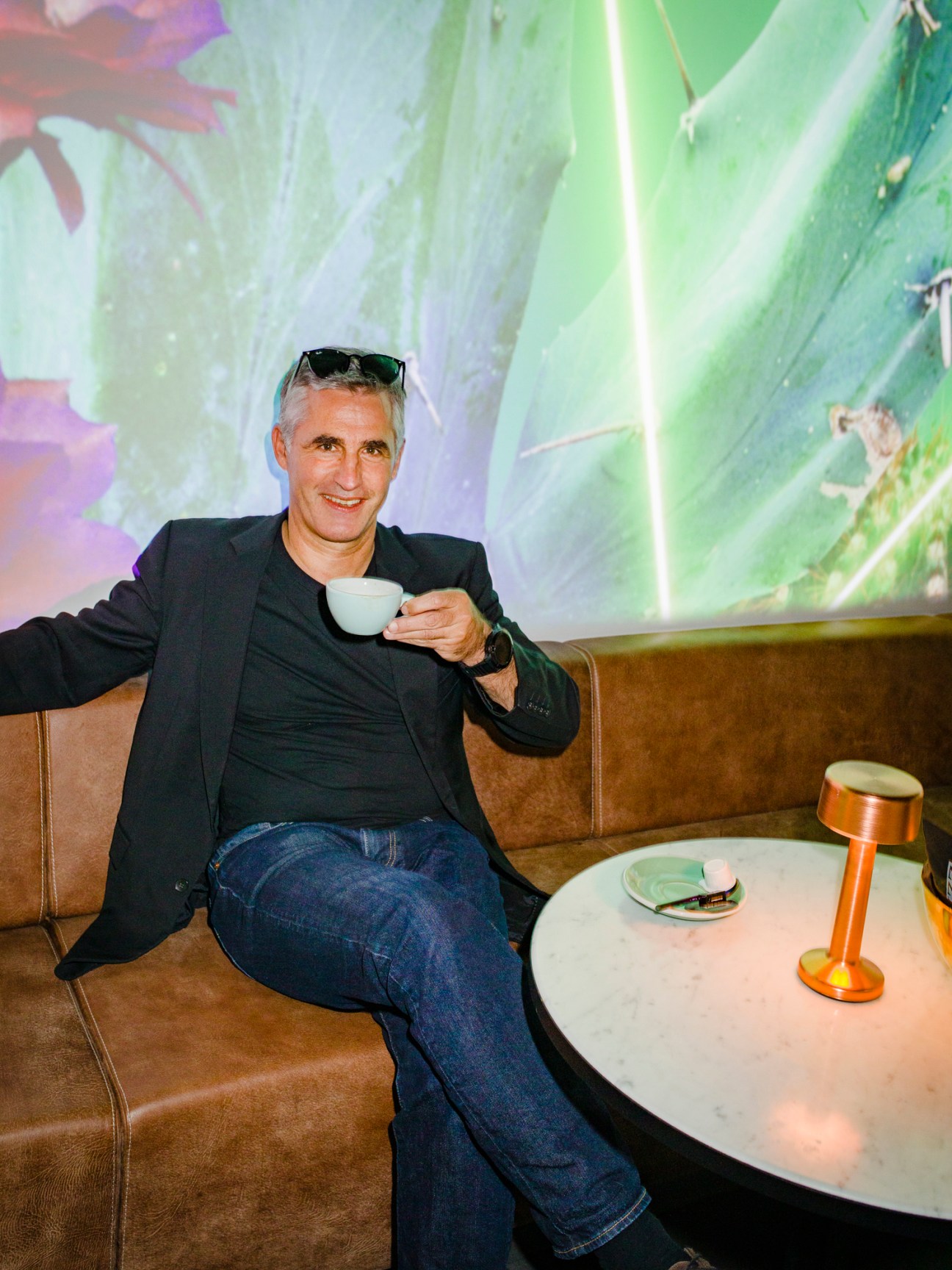 Man in dark blazer holding coffee cup at nzz am Bellevue with projected visuals on walls behind him
