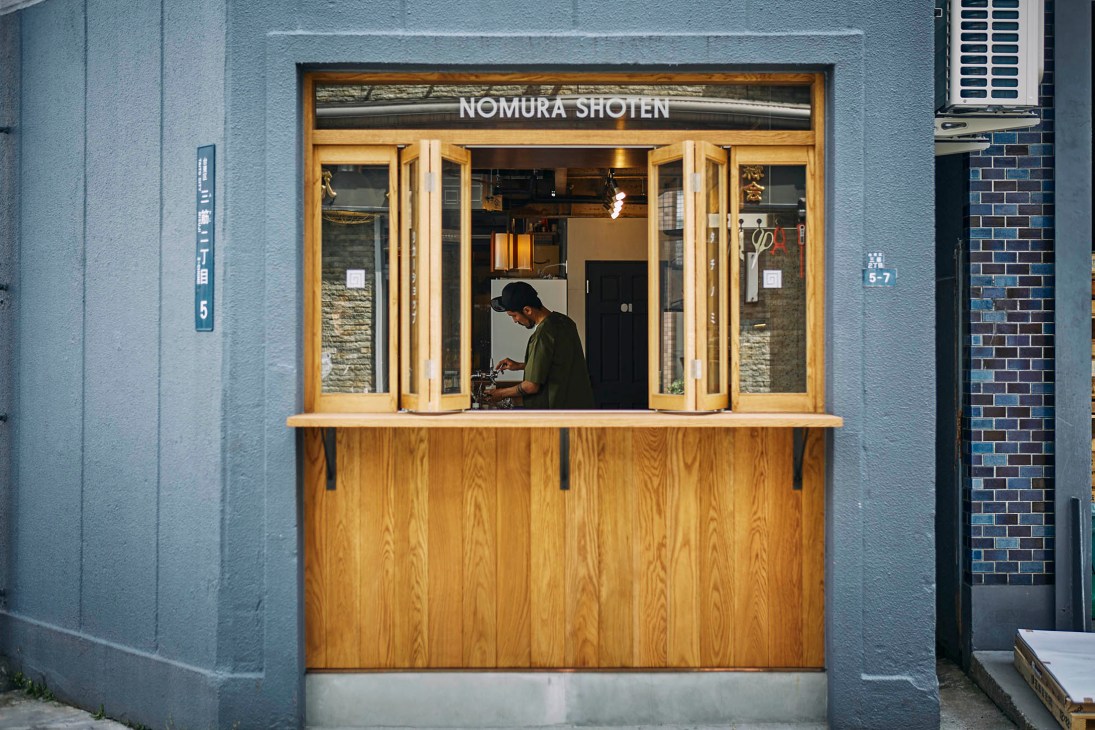 Minimalist wooden bar interior at Nomura Shoten with bottles displayed on shelves and service counter