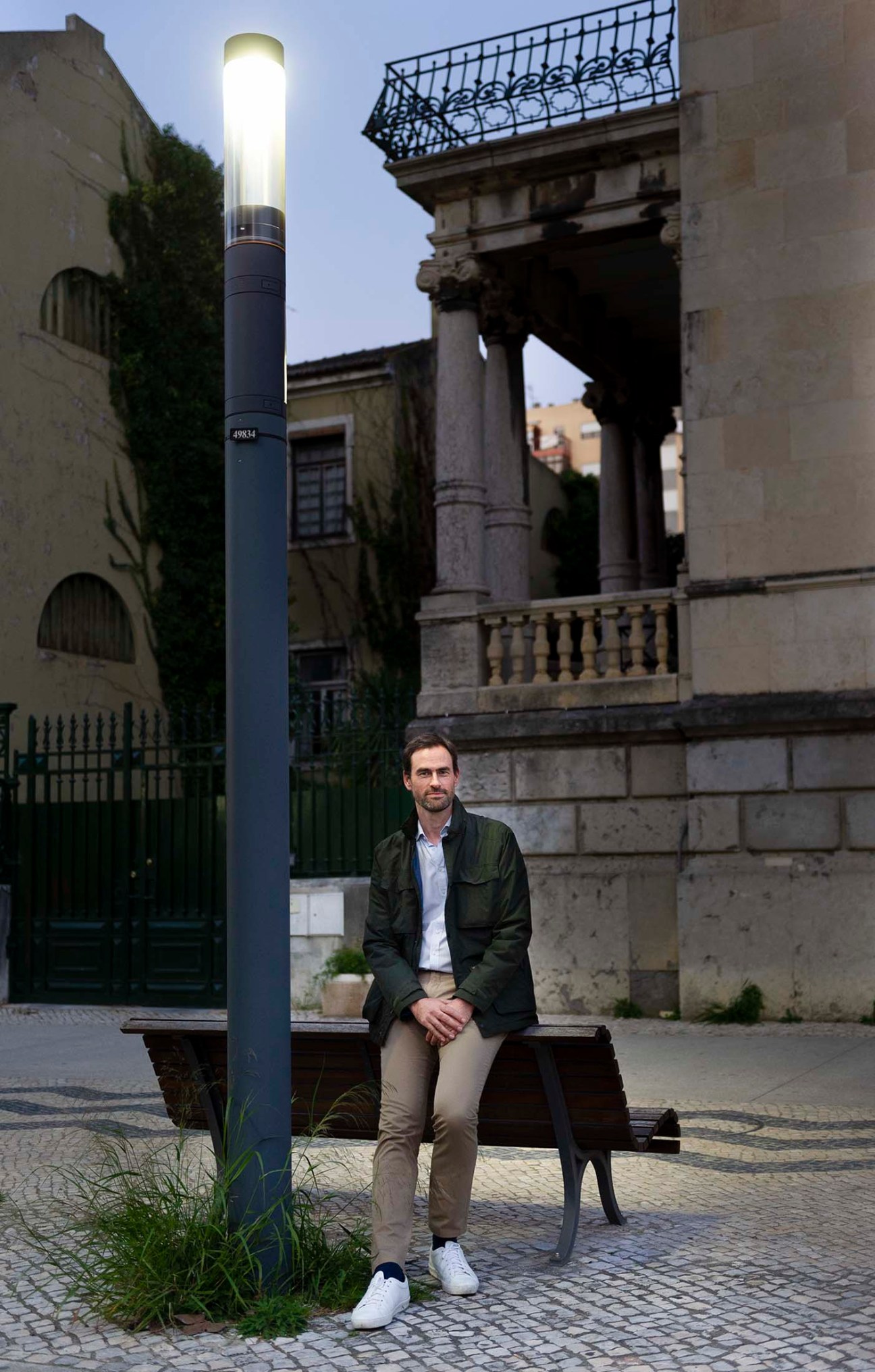 Nicolas Keutgen, chief innovation officer of lighting company Schréder, sits on a bench beneath an illuminated street lamp in a historic European plaza.