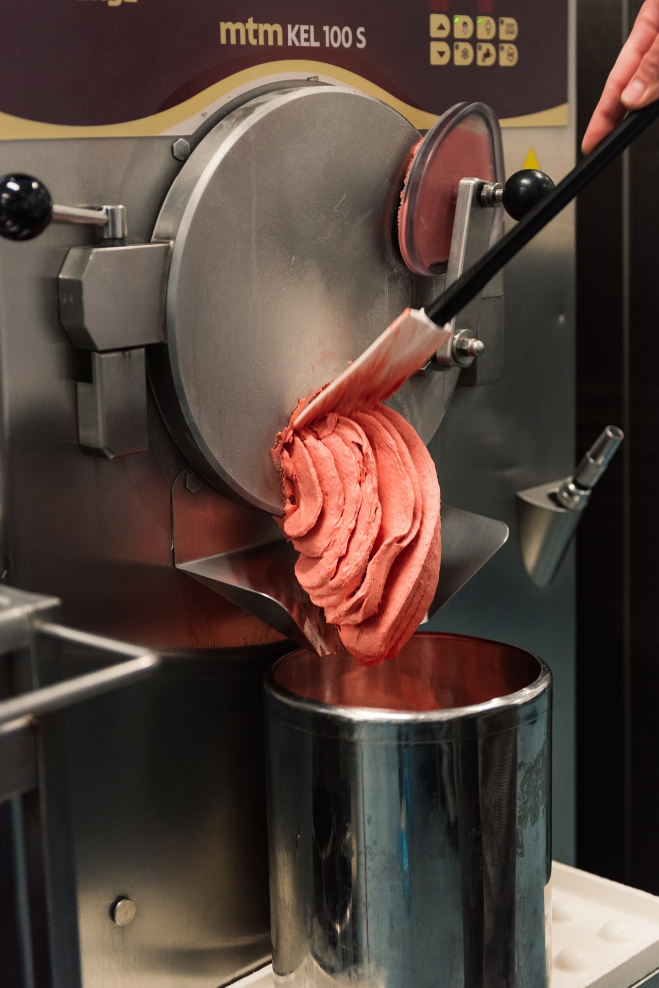 Pink gelato being dispensed from an MTM KEL 100 S machine into a metal container.