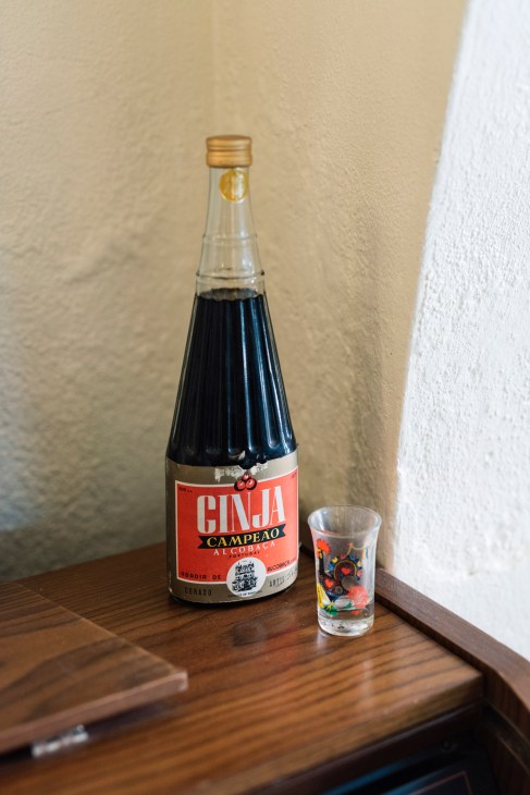 Bottle of Ginja Campeão Portuguese liqueur with glass on wooden piano surface against cream wall