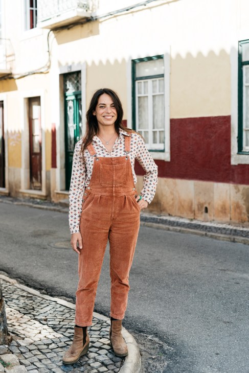 Raquel Ponte stands smiling on a Faro street lined with modernist buildings.