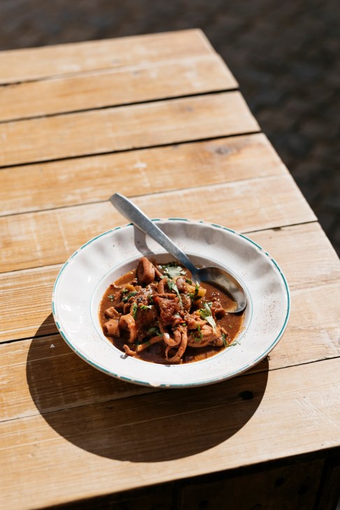 Bowl of stewed squid with herb garnish and spoon on wooden table at A Venda restaurant