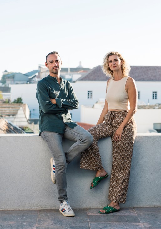 Christophe and Angelique de Oliveira sitting on a white wall overlooking Faro's white buildings.