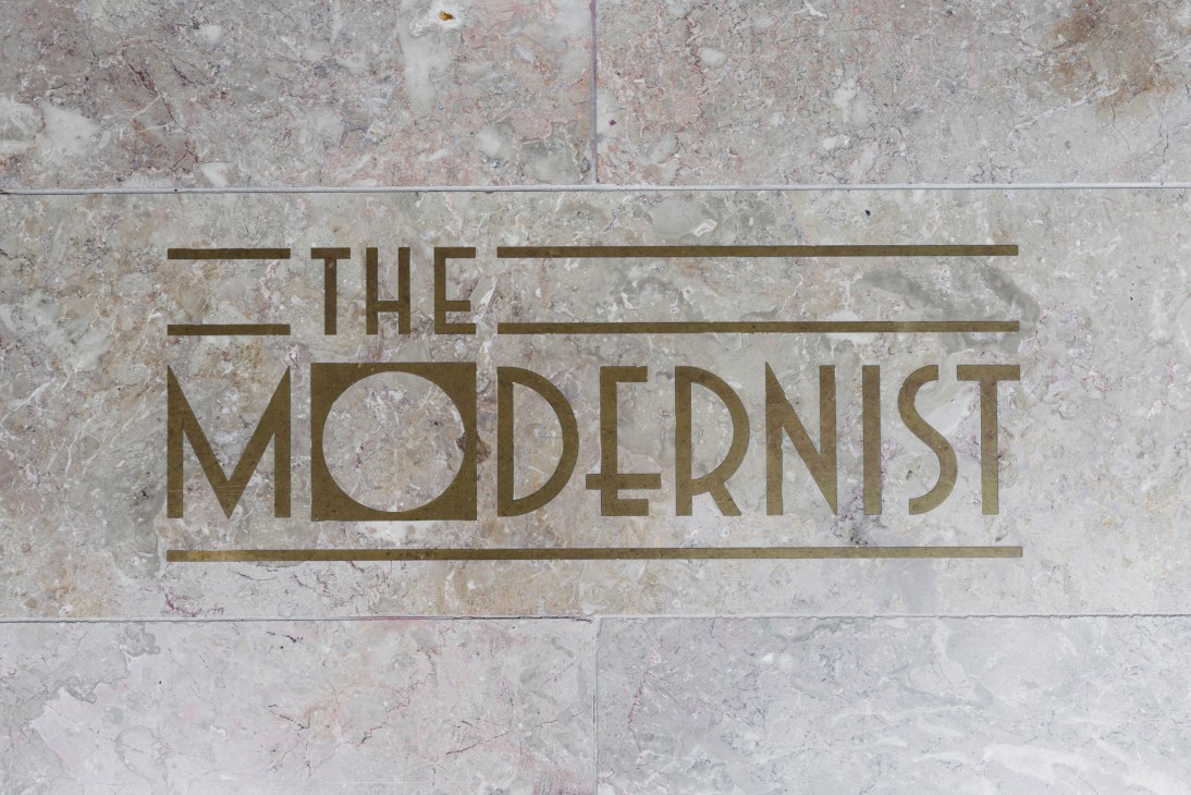 Gold lettering reading 'The Modernist' on a travertine tile surface