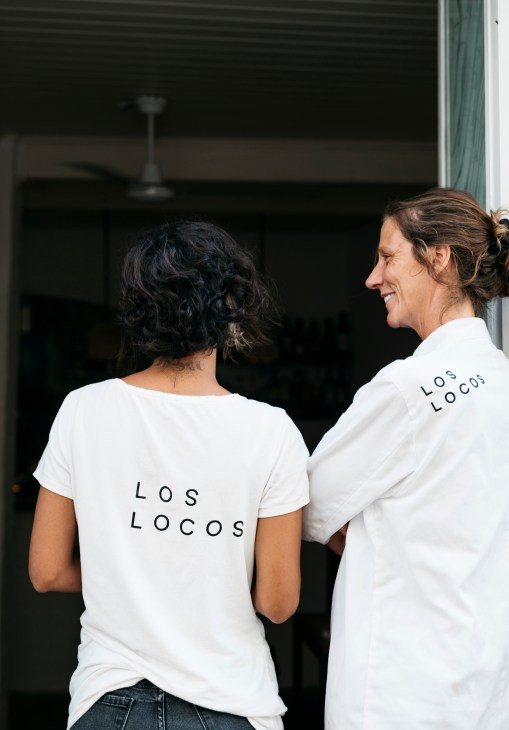 Two staff members wearing Los Locos restaurant t-shirts stand at the restaurant entrance.