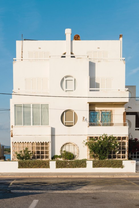 White modernist beach house with circular window details and geometric design against clear blue sky.
