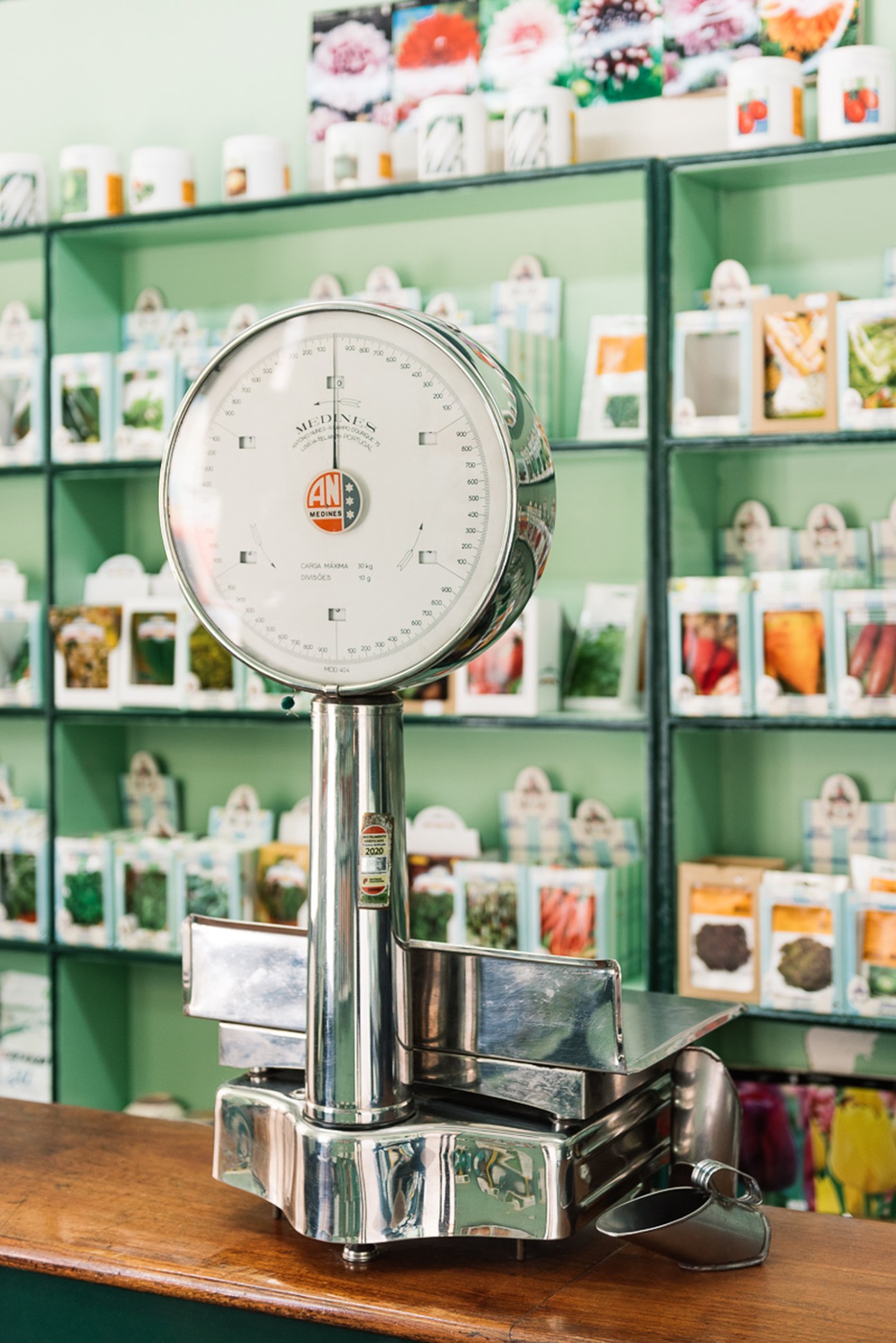 Chrome weighing scale with round dial display in a traditional Portuguese seed shop with colorful packets on shelves