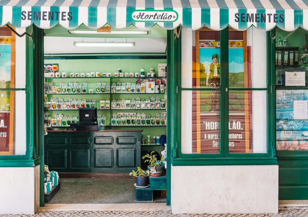Traditional Portuguese seed shop storefront with green and white striped awning displaying Sementes signs
