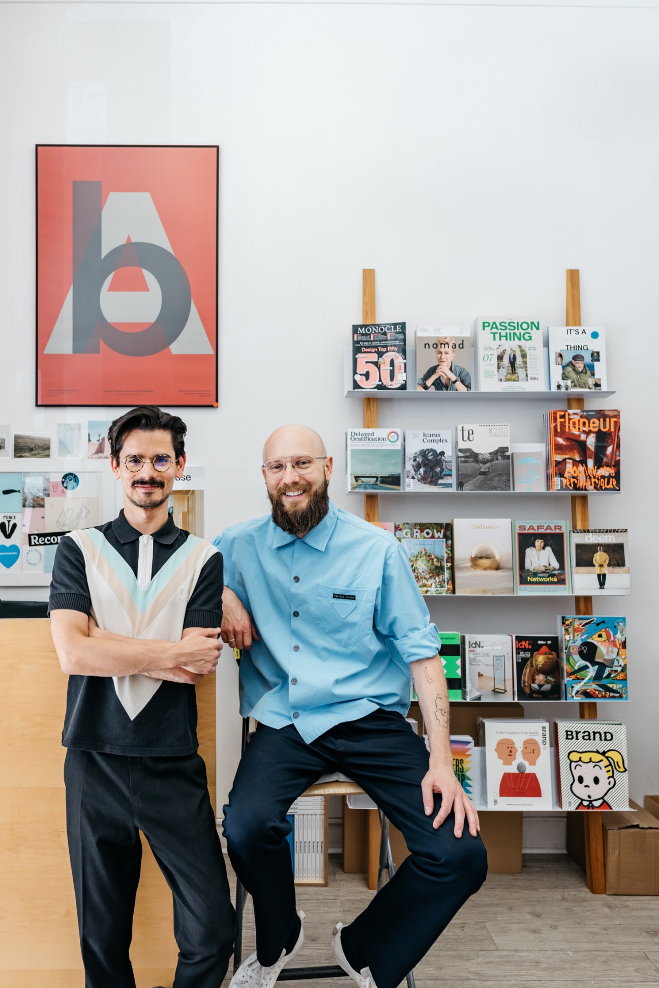 Two men standing in a magazine shop with display shelves of publications behind them