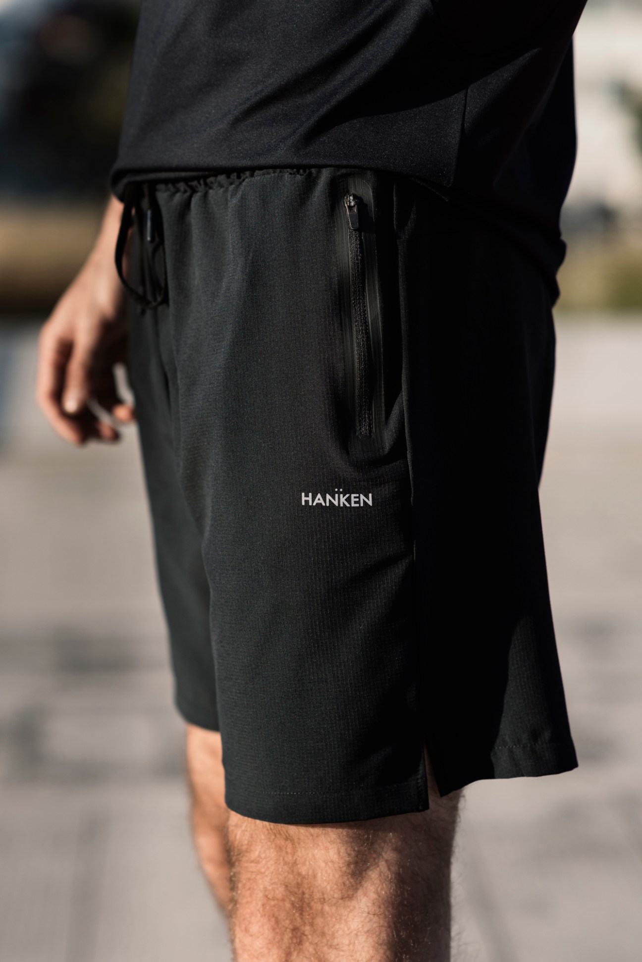 Black athletic shorts with zippered pocket worn by person, showing Hanken brand logo on leg