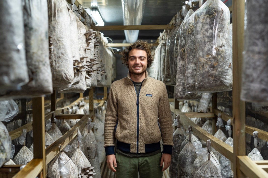 Natan Jacquemin standing in mushroom growing facility with bags of coffee ground substrate on shelves