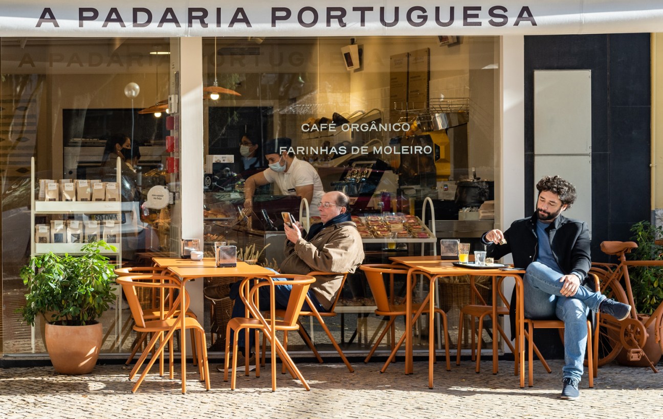 Outdoor seating area of A Padaria Portuguesa cafe with wooden chairs and tables on cobblestone street