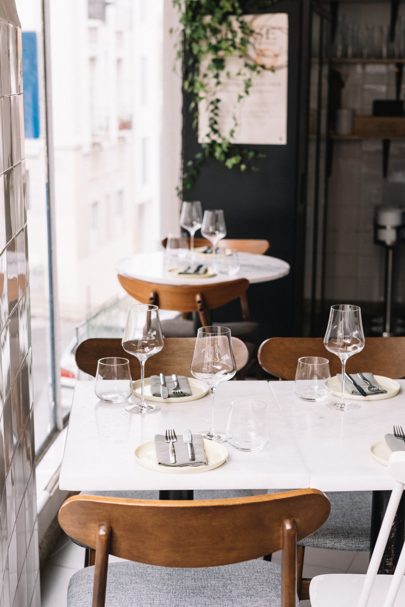 Restaurant interior with white marble tables, wooden chairs, wine glasses and place settings at Senhor Manuel