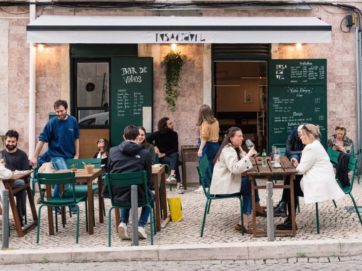 People dining at outdoor tables with green chairs outside Insaciável wine bar in Lisbon