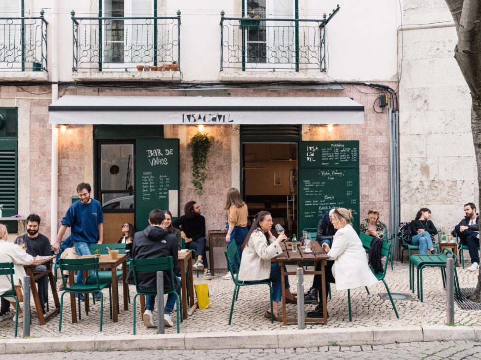 People dining at outdoor tables with green chairs outside Insaciável wine bar in Lisbon
