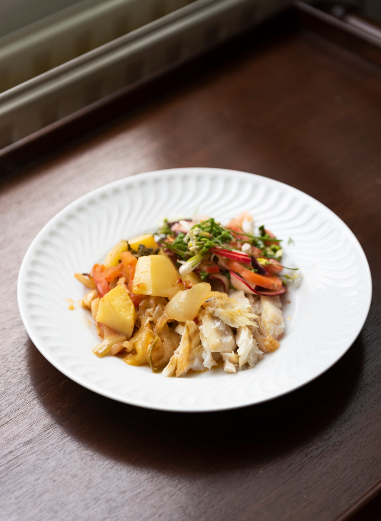 Plated turbot dish with potatoes and fresh herbs on white ridged plate