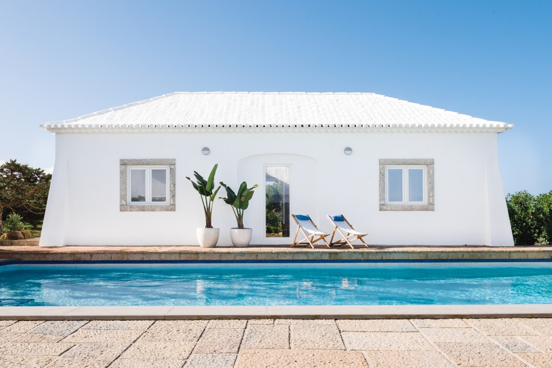 White modern pool house in Sintra with two blue deck chairs by the pool and potted plants.