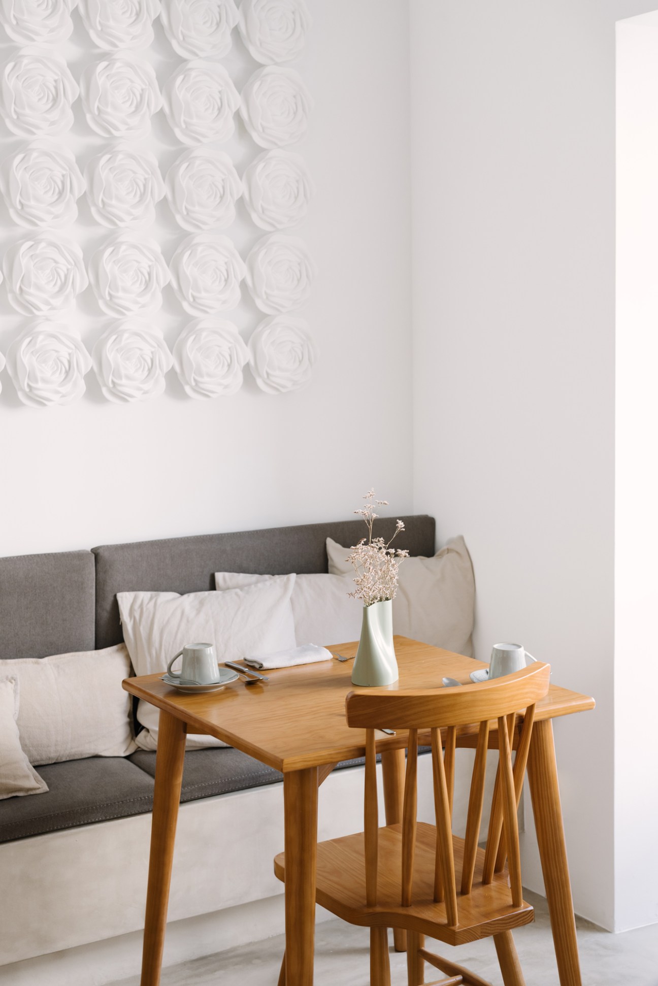 Hotel room interior with white textured rose-pattern wallpaper, grey upholstered bed and wooden side table