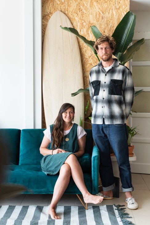 Amy Ilic and David Pentland, founders of Kelp Cowork, posing indoors with a surfboard and plant behind them.