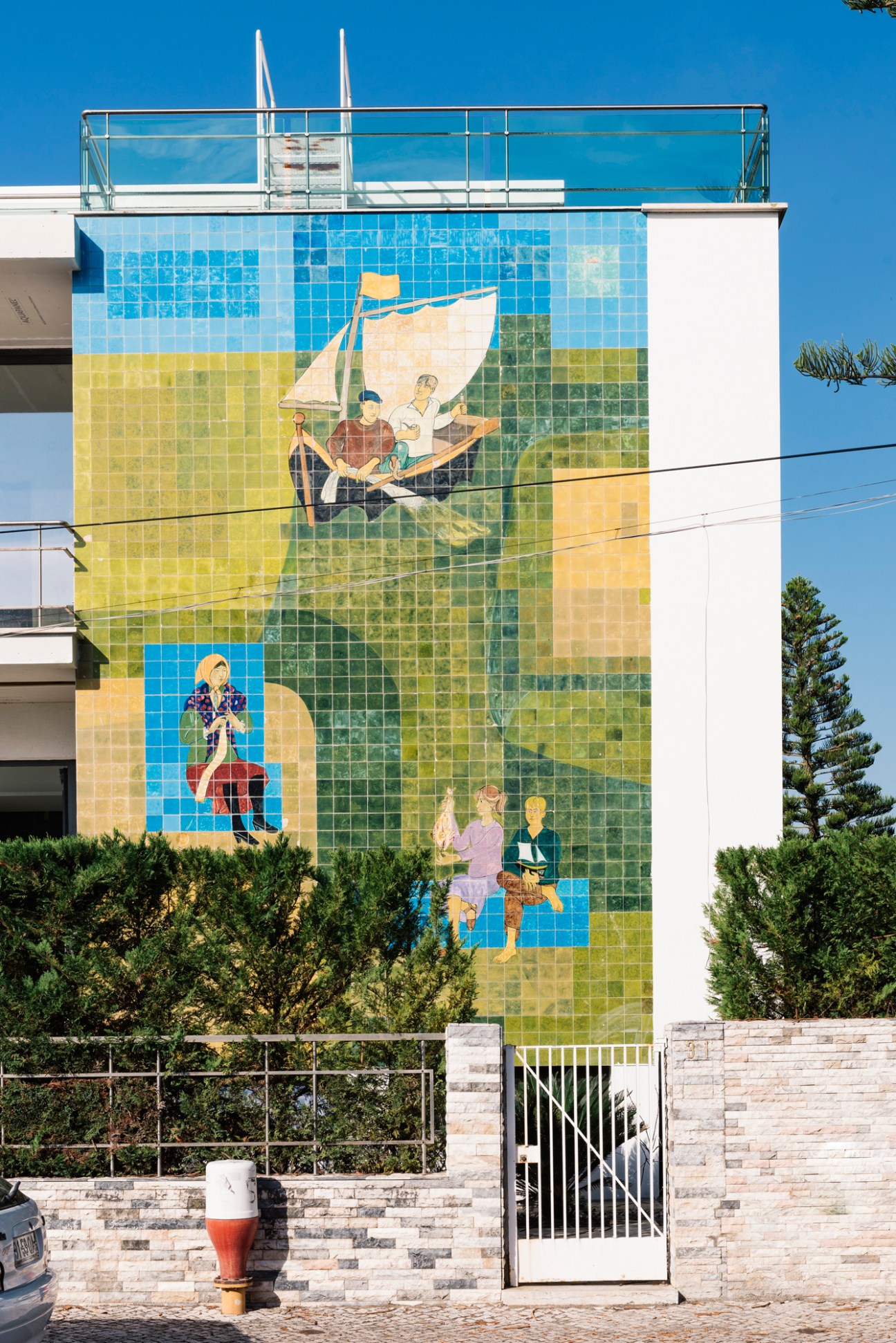 Colorful tiled mural on building wall depicting people with boats in blue, green and yellow mosaic pattern