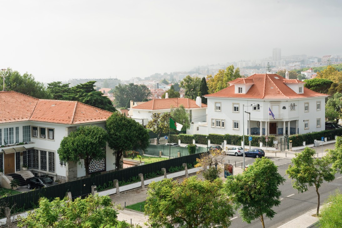 Leafy residential street in Restelo, Lisbon with white buildings, red tile roofs, and lush green trees