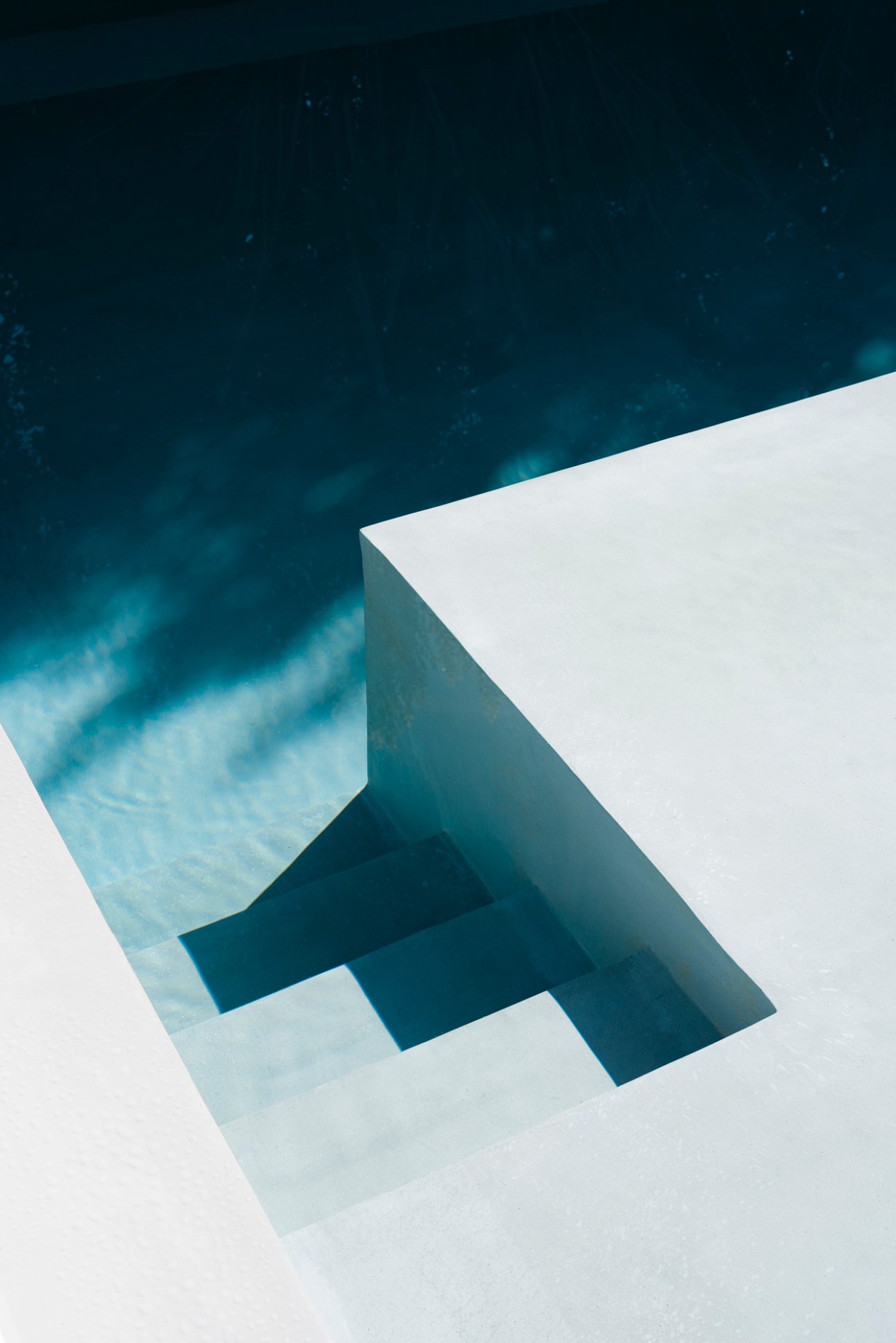 White geometric architectural structure casting angular shadows against deep blue sky and clouds