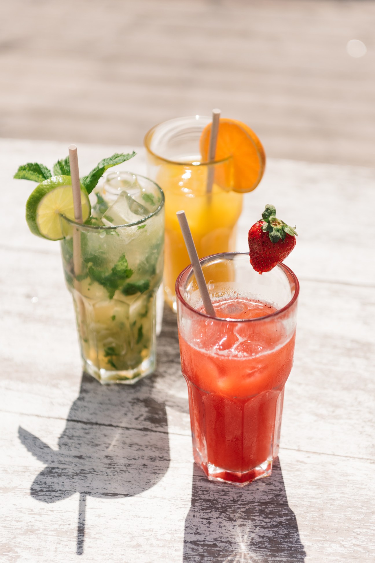 Three colorful cocktails on a white surface with lime, orange and strawberry garnishes.