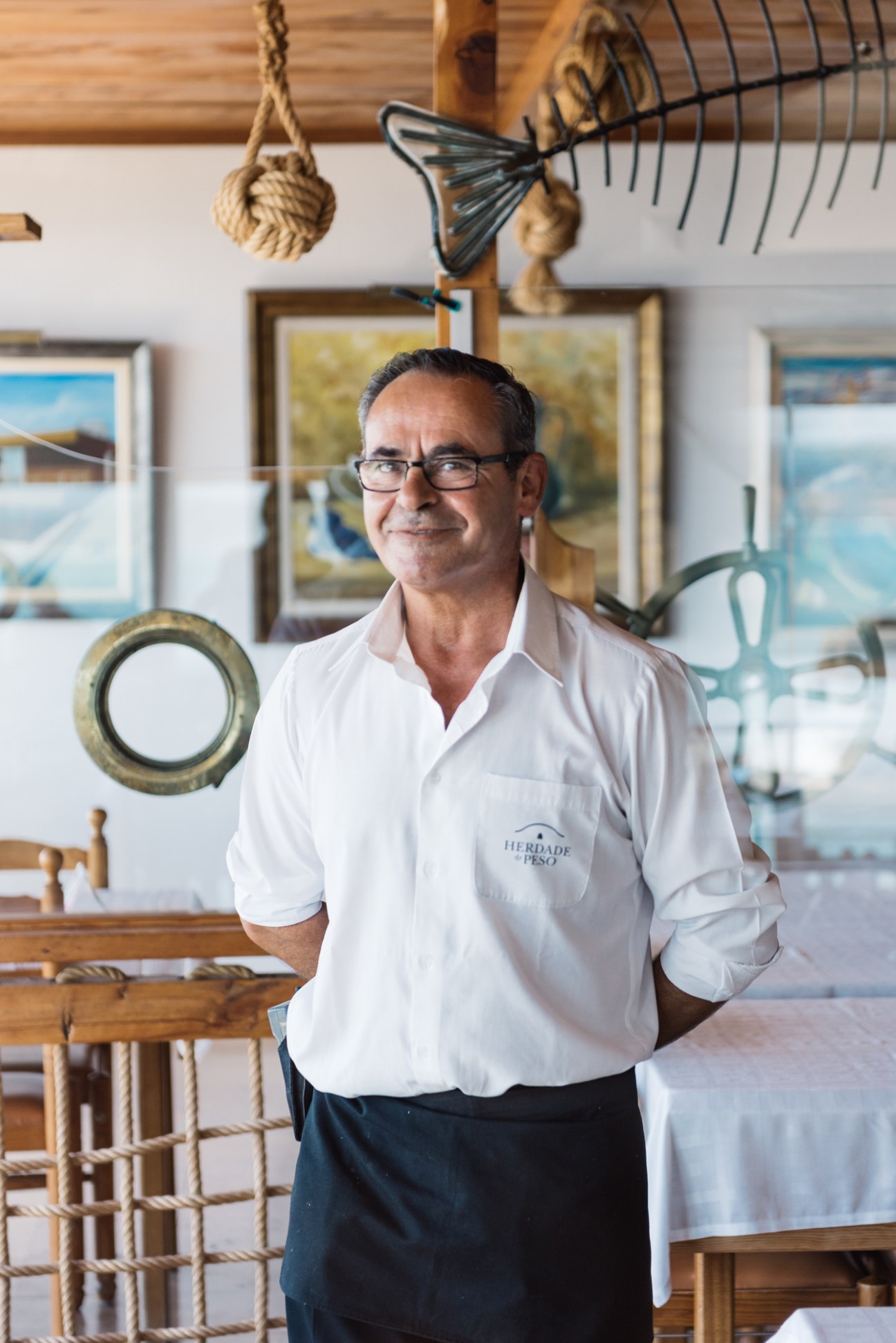 Raul Dias, a waiter at Esplanada das Furnas, stands in the restaurant's nautical-themed interior decorated with maritime objects.
