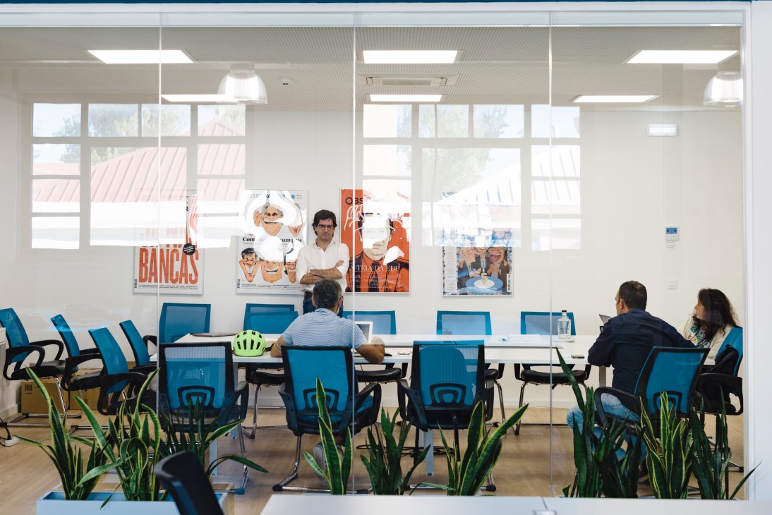 Observador staff members meet at a conference table in a bright, modern office with blue chairs and magazine covers on the wall.