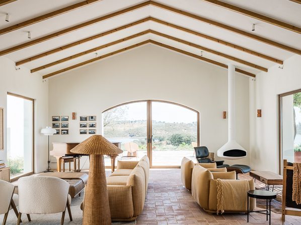 Modern living room with exposed wooden beams, terracotta tiles, neutral furniture and large arched doorway