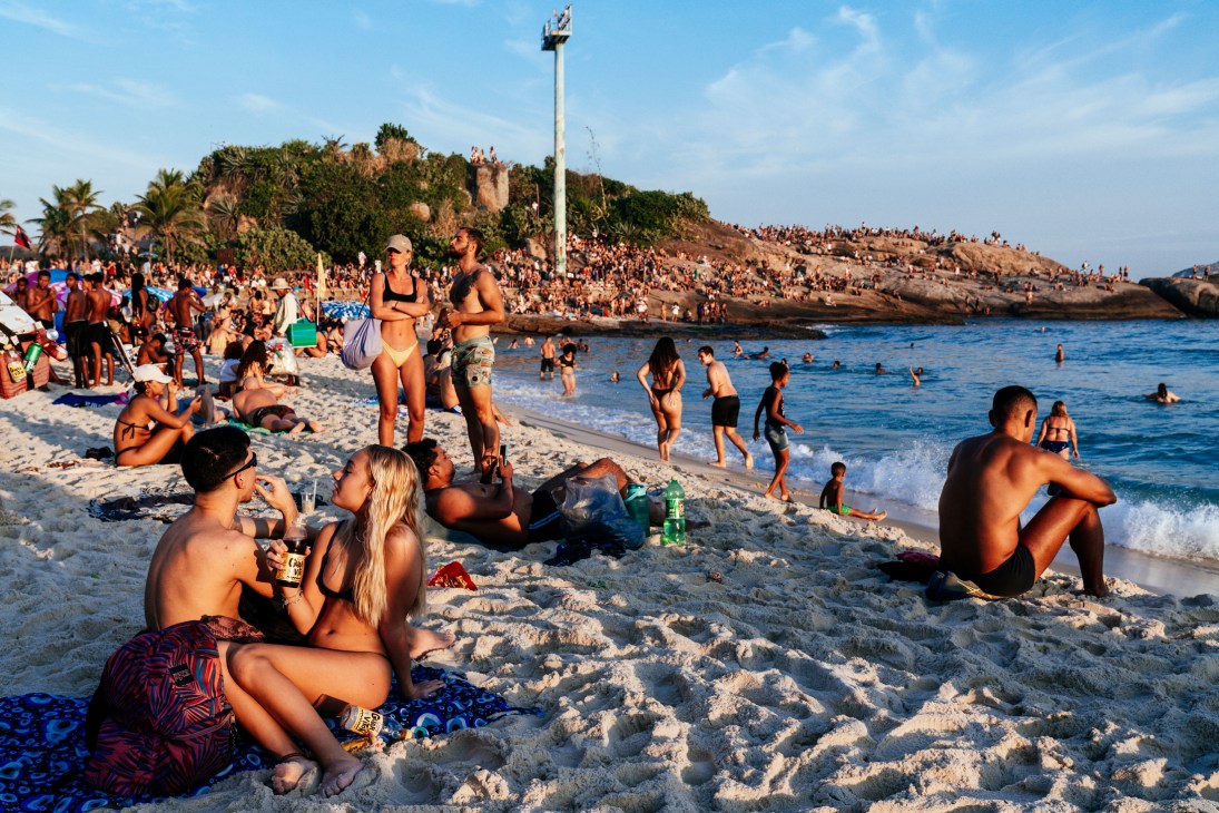 Crowded beach scene with people in swimwear relaxing on white sand near blue ocean waters at sunset