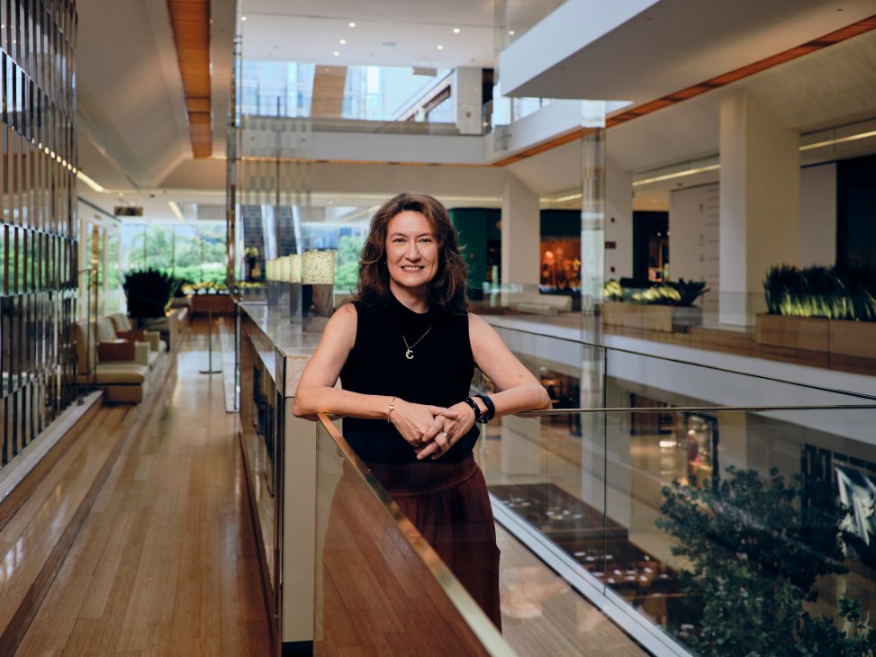 Woman in black sleeveless top standing on a modern multi-level corridor with glass railings, skylights, and contemporary architectural design