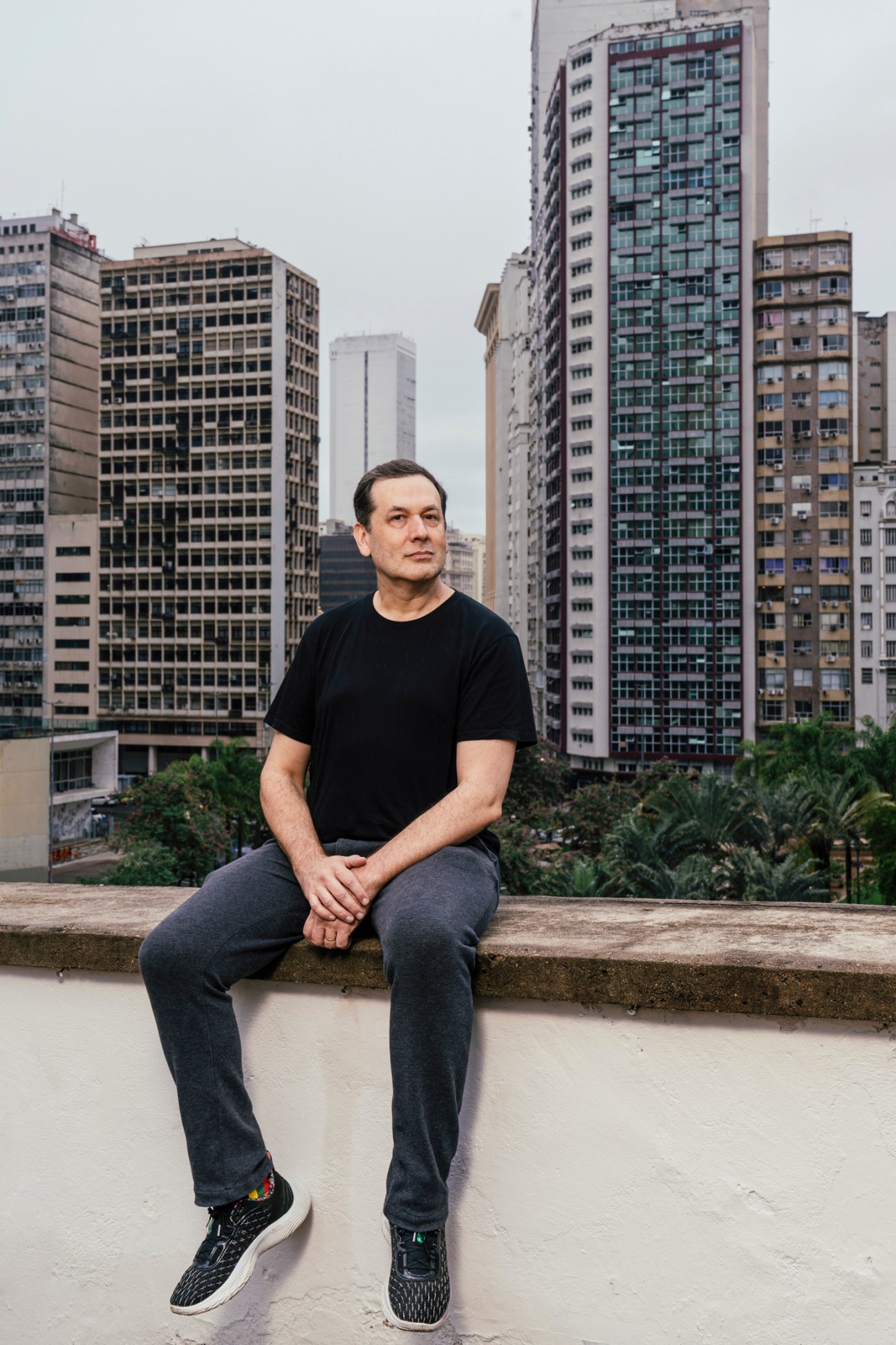 Washington Fajardo sits on a concrete ledge with urban buildings and greenery in the background