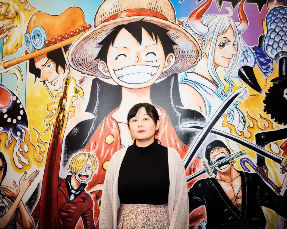 Satoko Inaba, editorial director of manga at Glénat, standing in front of colorful One Piece manga artwork