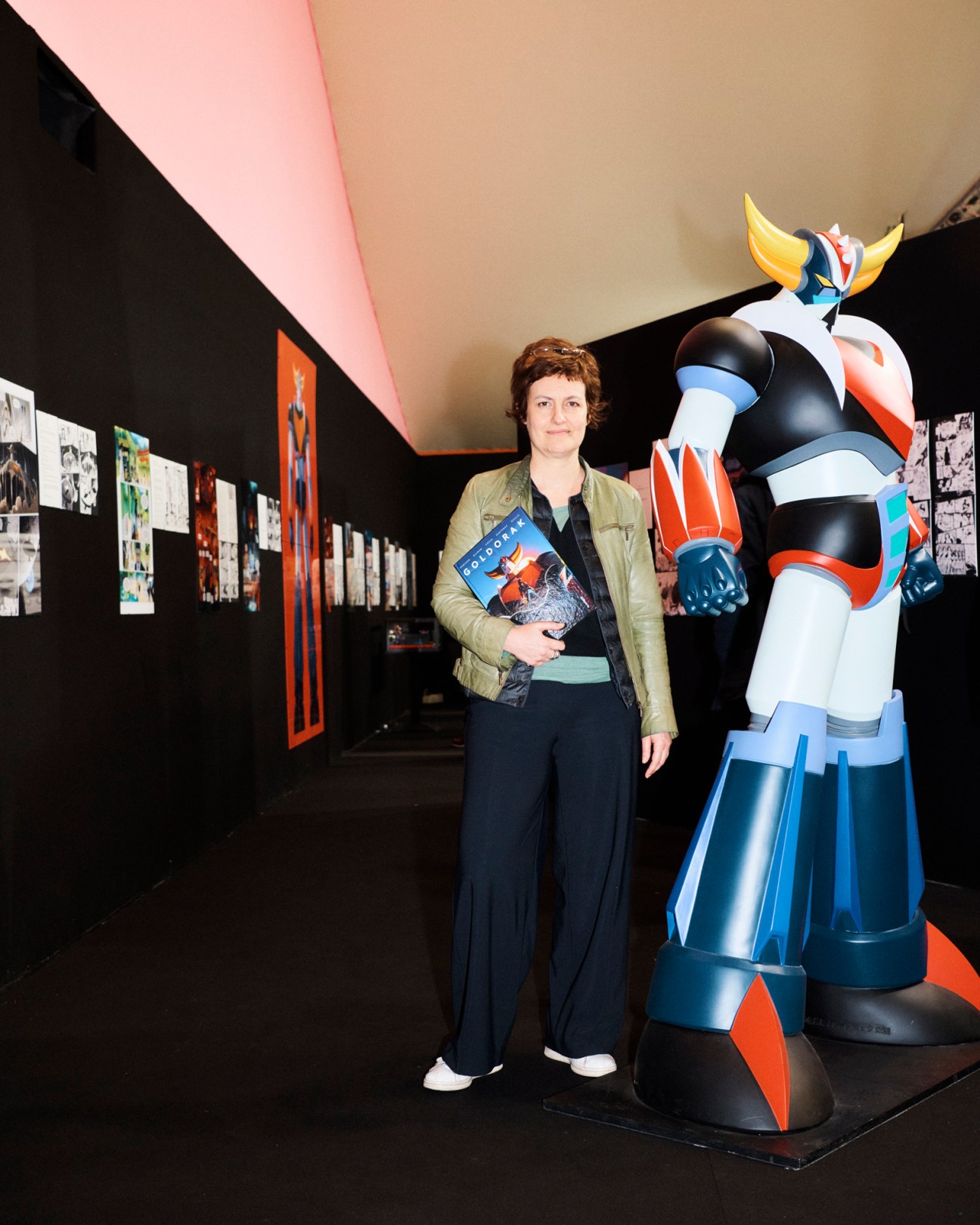 Christel Hoolans stands next to a large anime character statue in an exhibition space with comic artwork on walls